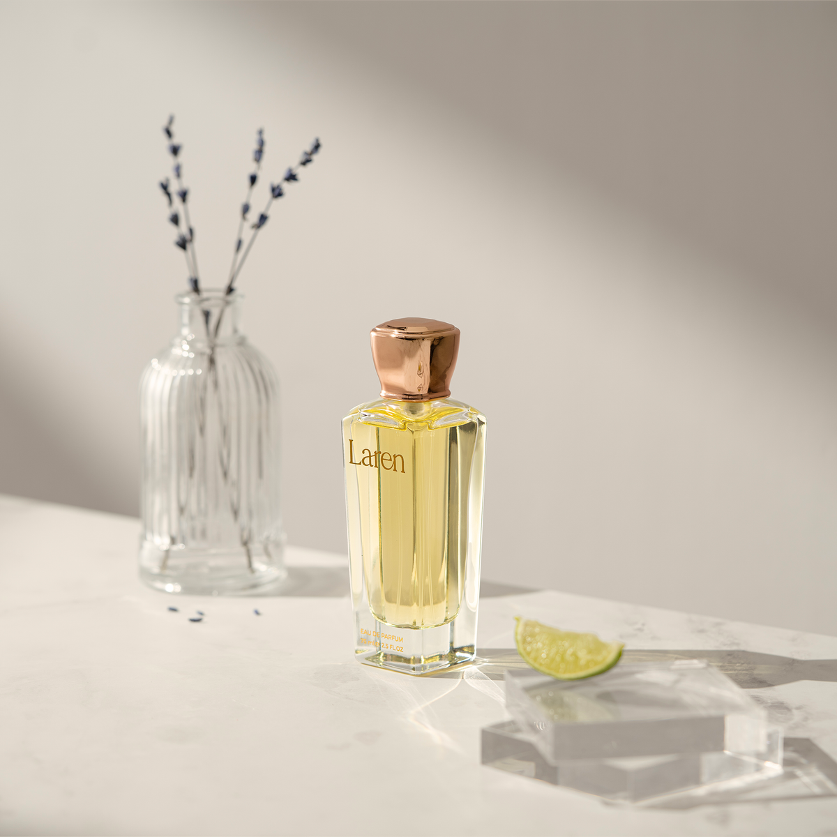 عطر لارين على سطح رخامي بجانب مزهرية زجاجية فيها لافندر وشريحة ليمون على مكعب شفاف