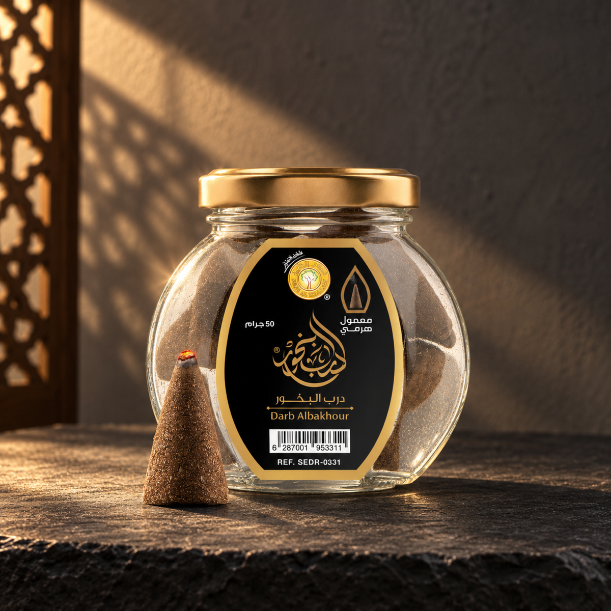 معمول هرمي درب البخور 50 جرام من سدر الخليج؛ عبوة زجاجية بملصق أسود وغطاء ذهبي ومعها مخروط واحد على حجر أسود في ضوء شمس مائل.
