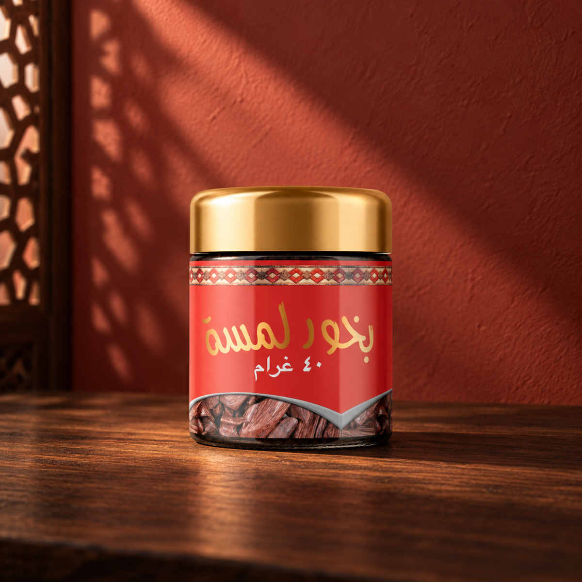 بخور لمسة 40 جرام من سدر الخليج؛ برطمان بغطاء ذهبي وملصق أحمر على خشب أمام جدار أحمر في ضوء الشمس.