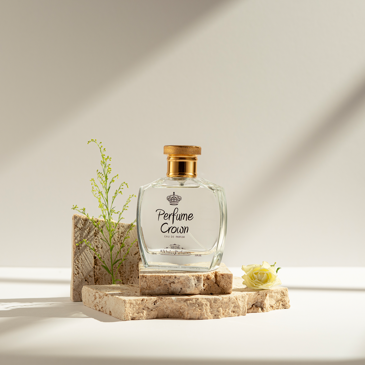 Perfume Crown 100 ml on stone slabs beside a plant sprig and a yellow flower in sunlight