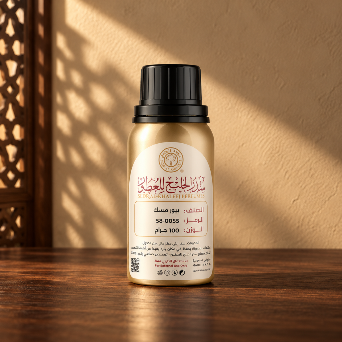 عطر زيتي بيور مسك من سدر الخليج؛ عبوة معدنية ذهبية بغطاء أسود وملصق كريمي فوق خشب جوز، أمام جدار رملي مع شمس مائلة وظل مشربية.