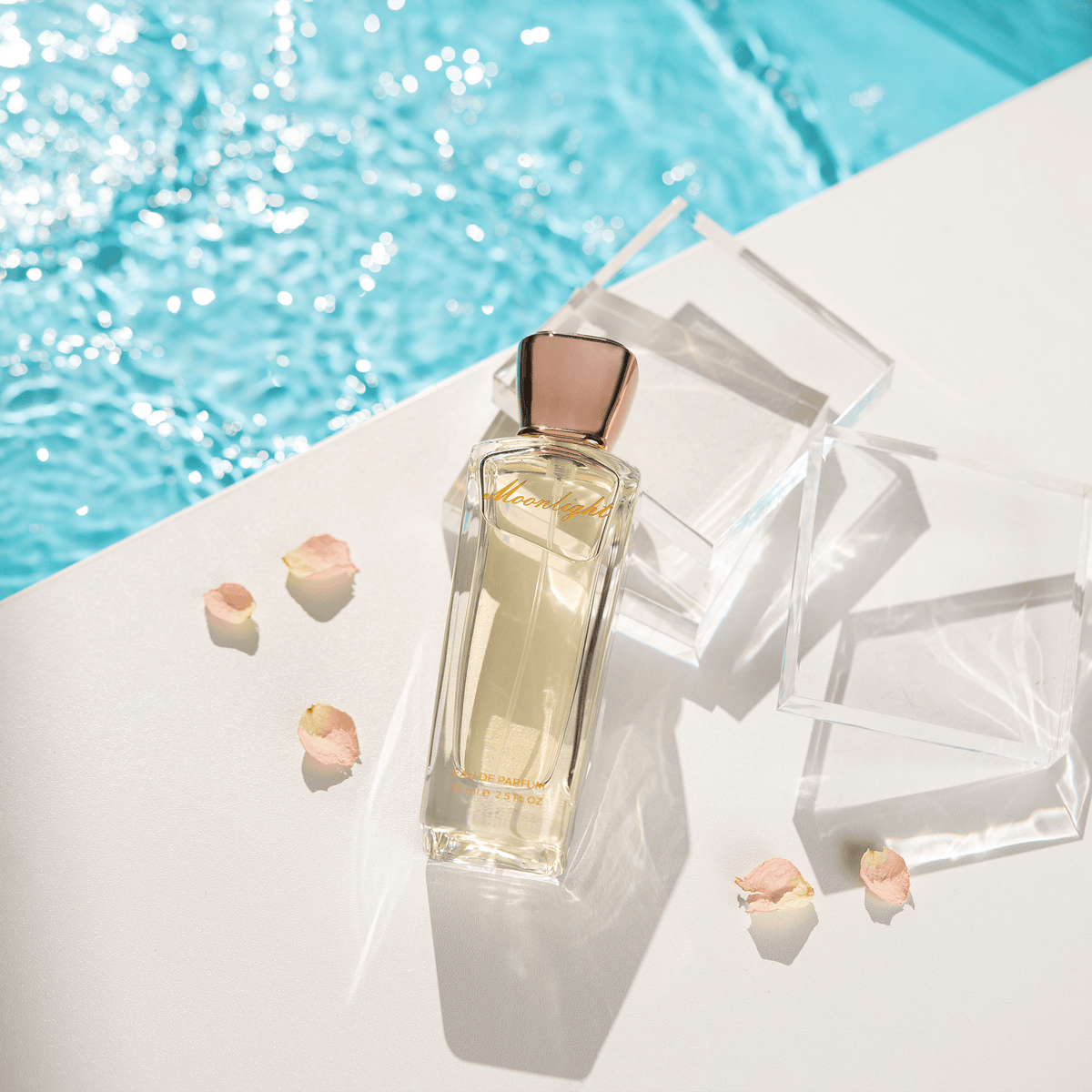 Moonlight Perfume on a white ledge by blue water with clear blocks and rose petals