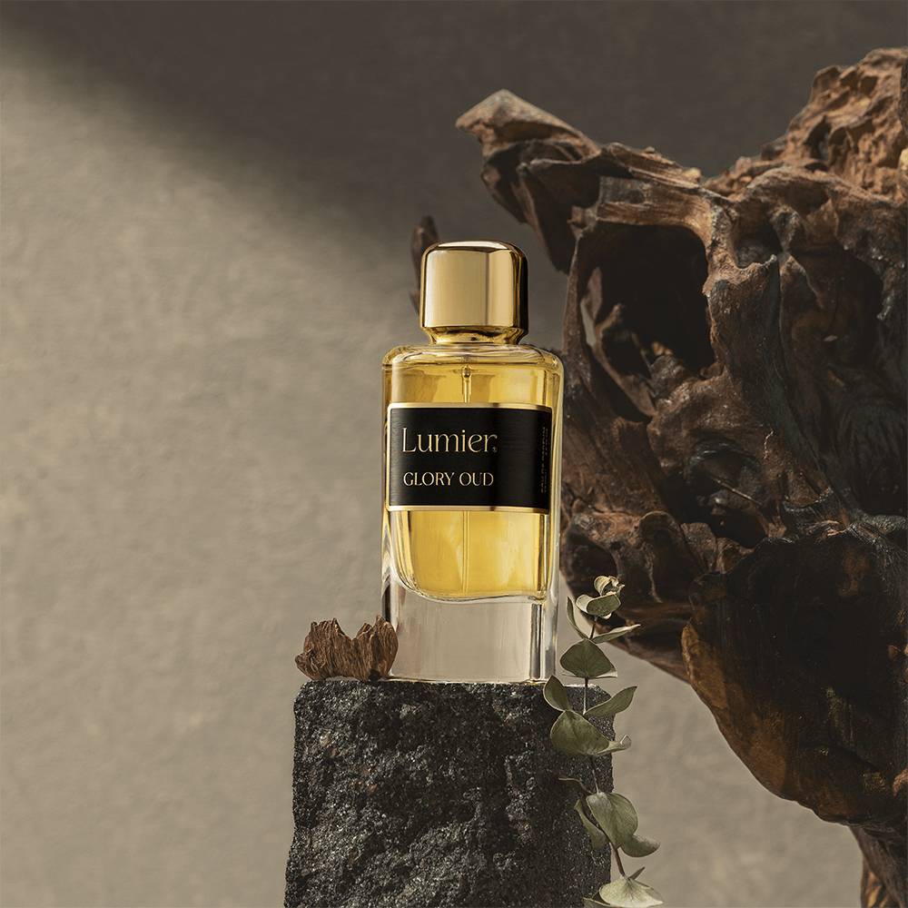 Glory Oud Perfume 75 ml on a dark rock beside a piece of oud wood and a eucalyptus sprig on a grey background