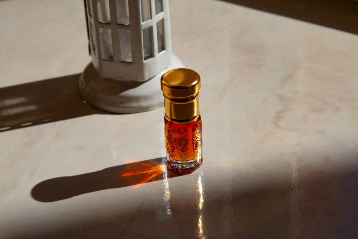 قارورة عطر زيتي صغيرة بغطاء ذهبي على سطح رخامي يقع عليه ضوء الشمس