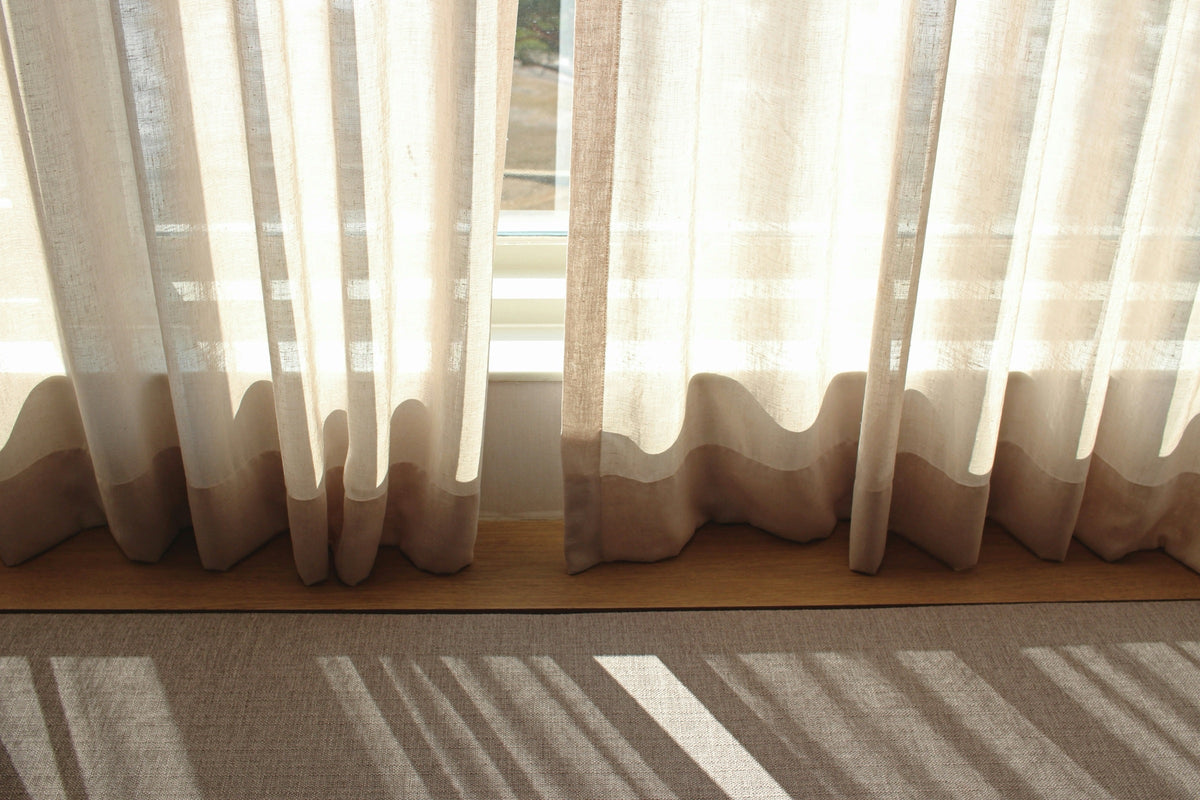 Light white linen curtains on a window letting in daylight, with their shadows on the floor