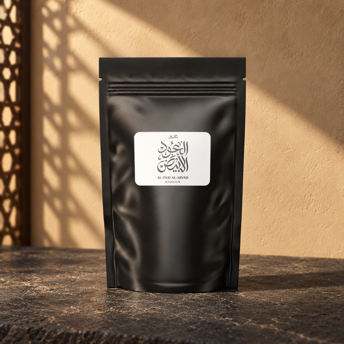 Al Oud Al Abyad Bakhoor by Weight from Sedr Al-Khaleej; closed matte black pouch with a white label on basalt against a sand wall, with angled sunlight and a wooden screen shadow.