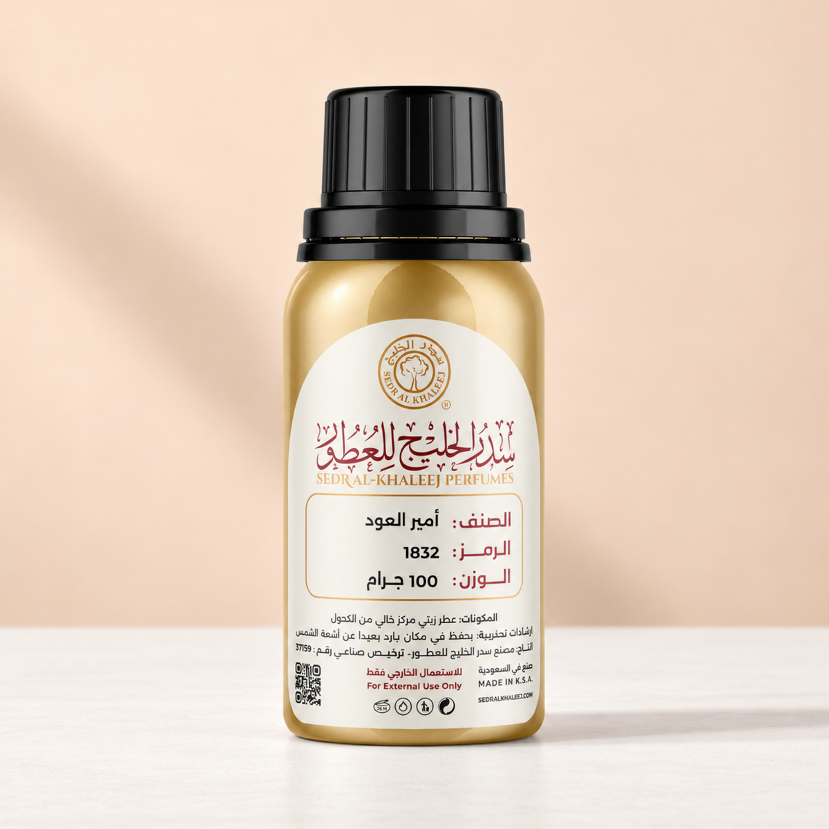 زيت عطري أمير العود من سدر الخليج؛ قارورة ذهبية على خزف أبيض أمام خلفية مشمشية فاتحة بإضاءة نهارية منتشرة