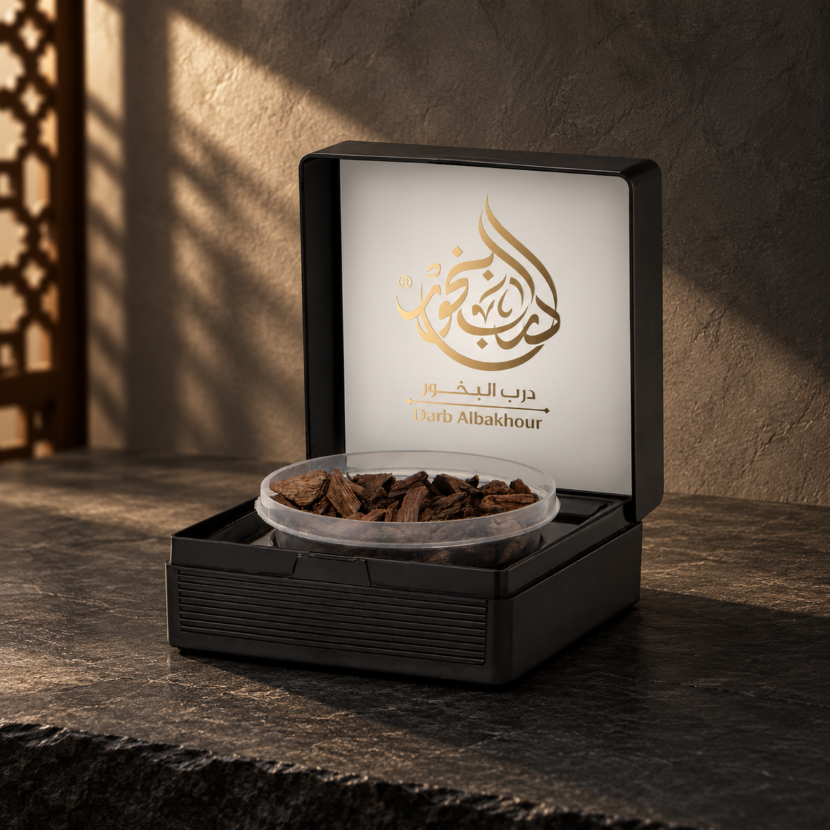 عود معطر درب البخور 50 جرام من سدر الخليج؛ علبة سوداء مفتوحة وبداخلها وعاء رقائق عود فوق حجر داكن، أمام جدار فحمي مع شمس مائلة وظل مشربية.