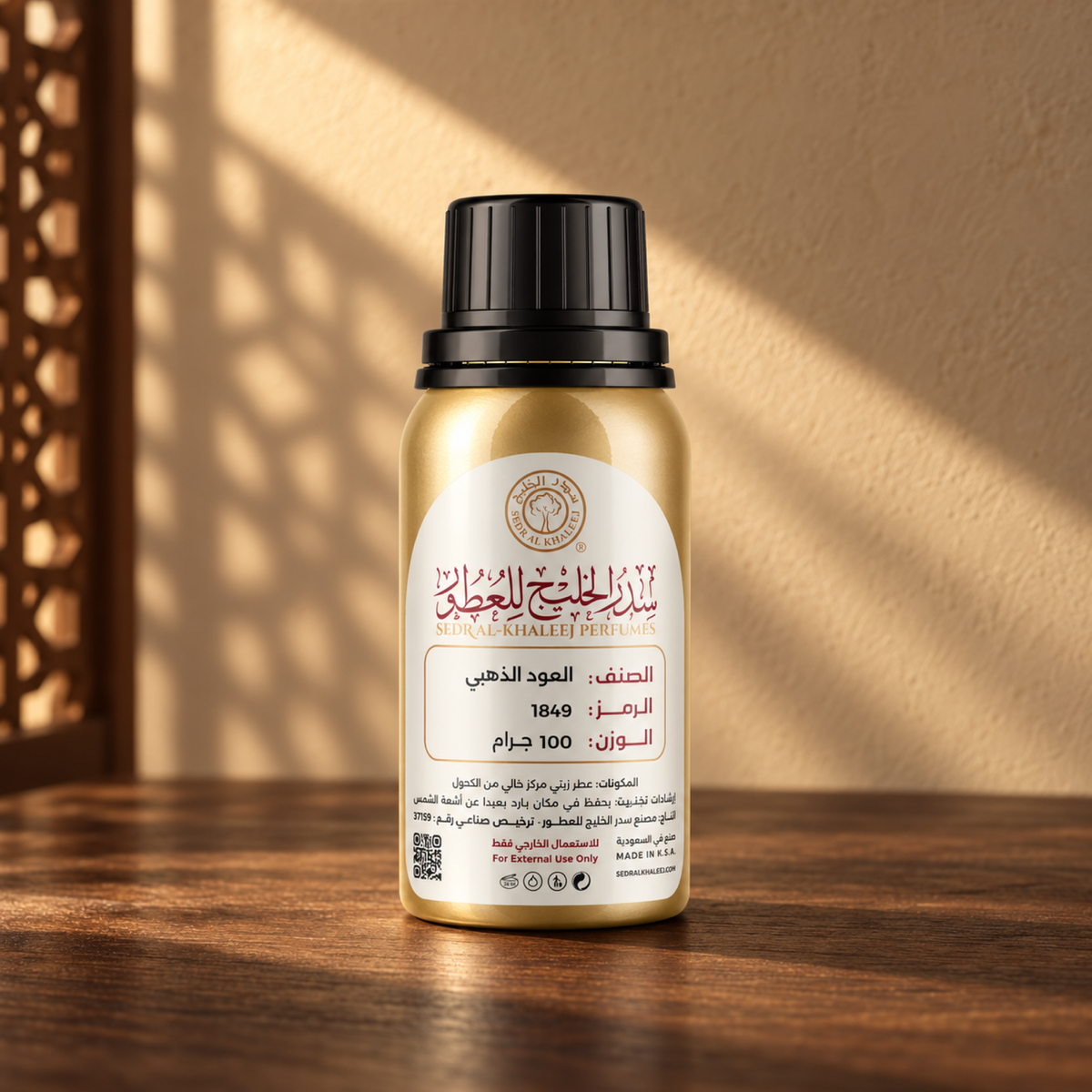 عطر زيتي العود الذهبي من سدر الخليج؛ عبوة معدنية ذهبية بغطاء أسود وملصق كريمي فوق خشب جوز، أمام جدار رملي مع شمس مائلة وظل مشربية.