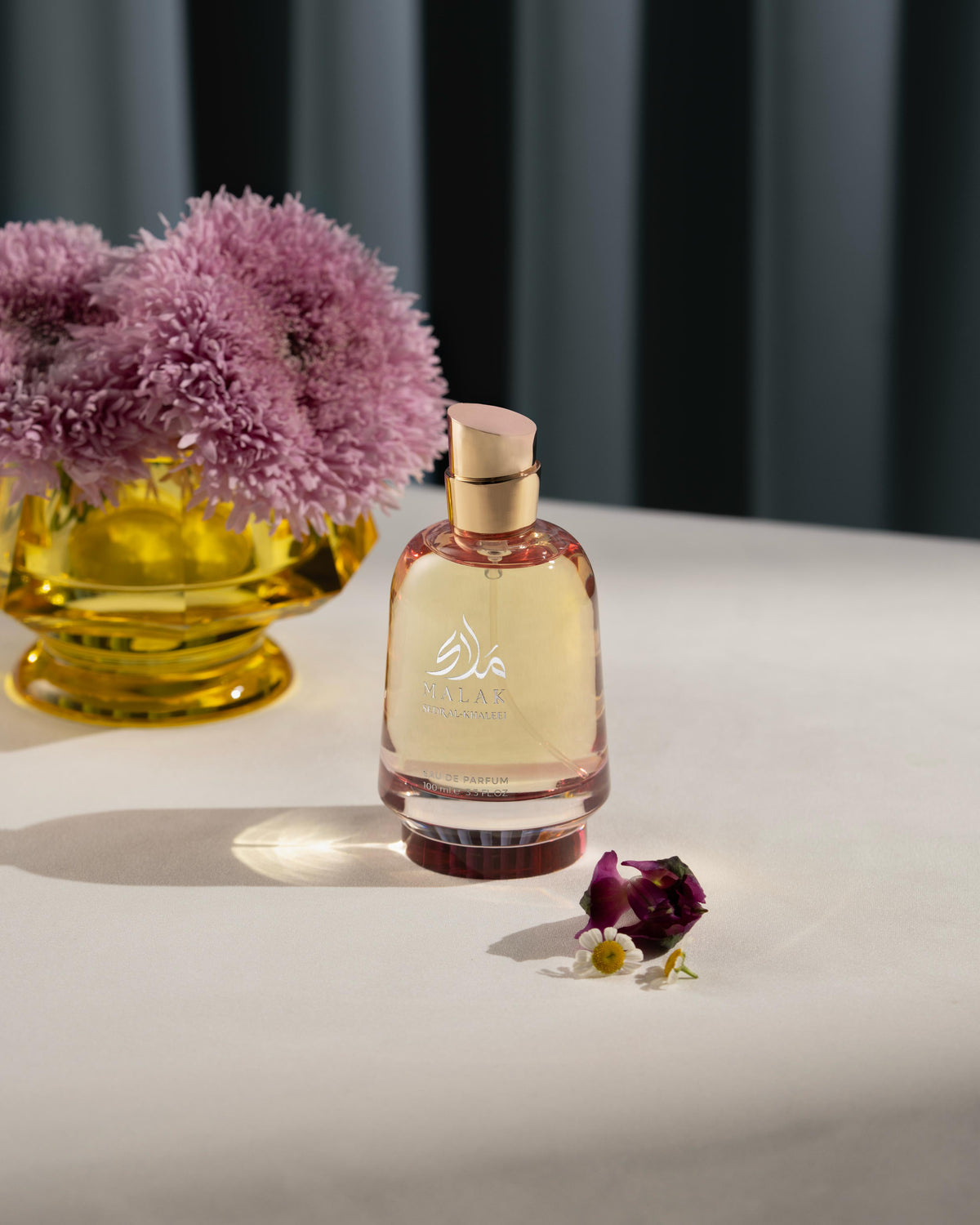 Malak perfume bottle on a table beside a flower vase