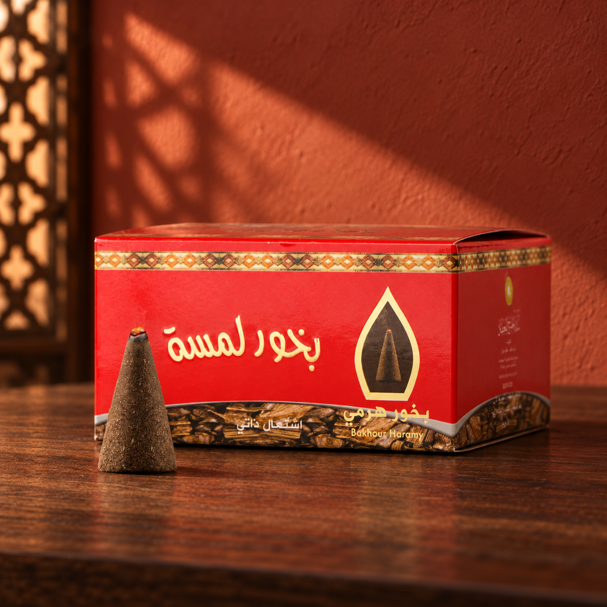Lamsa Pyramid Bakhoor 50 g from Sedr Al-Khaleej; red incense box with one cone on walnut wood against a muted brick-red wall in angled sunlight.