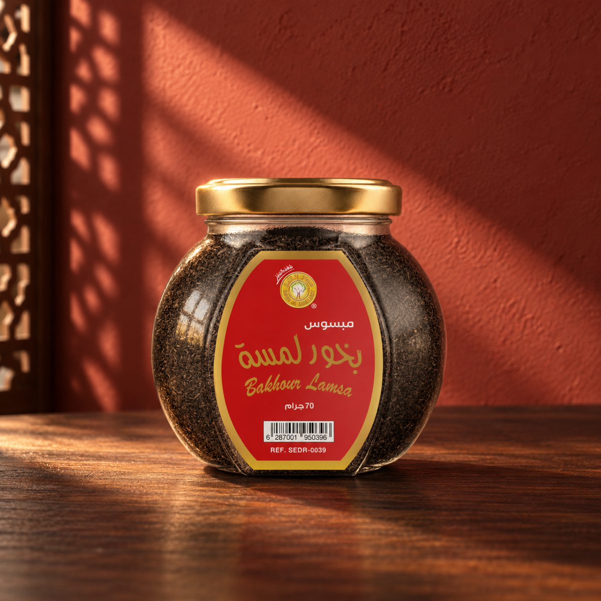 Lamsa Bakhoor Mabsos 70 g from Sedr Al-Khaleej; closed jar with a gold lid and red label on walnut wood against a brick red wall, with angled sunlight and a wooden screen shadow.