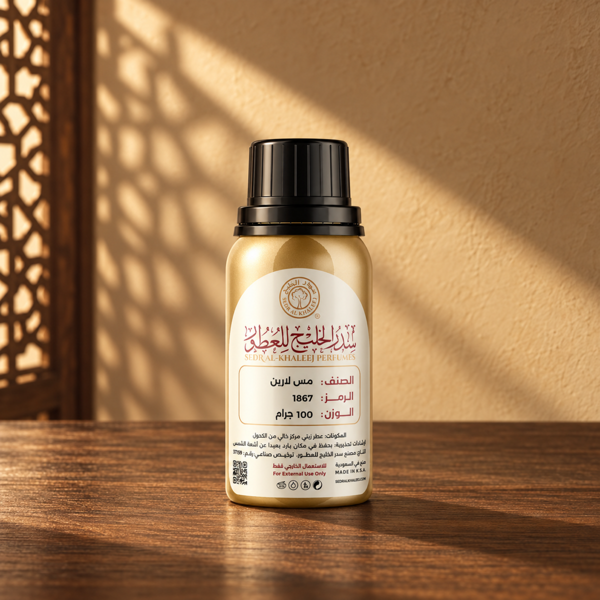 Sedr Al-Khaleej Miss Laren perfume oil in a gold bottle with a black cap and cream label on walnut wood against a sand plaster wall with sunlight and a mashrabiya shadow.