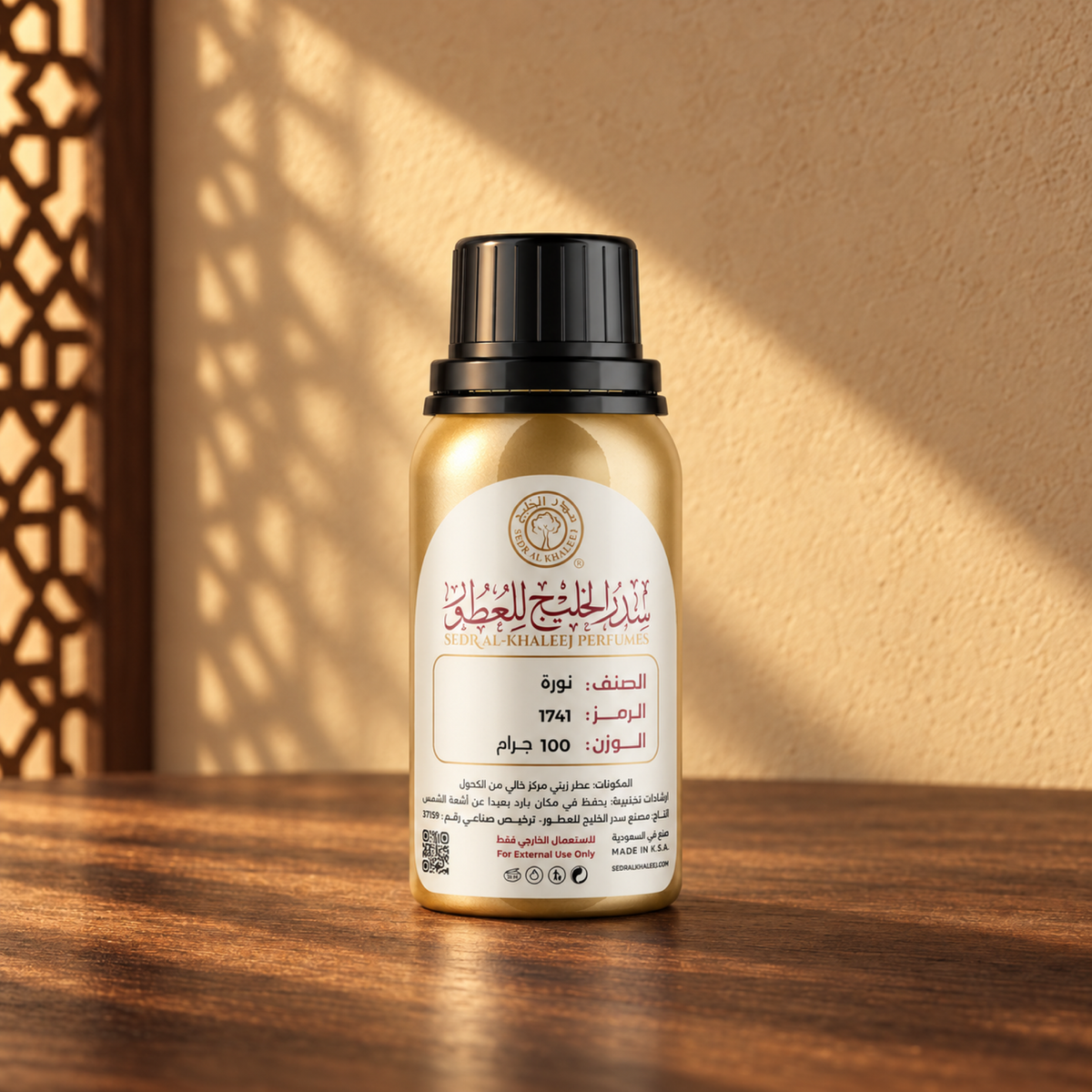 Sedr Al-Khaleej Noura perfume oil in a closed gold bottle with a black cap and cream label on walnut wood against a sand wall in sunlight beside a screen shadow.