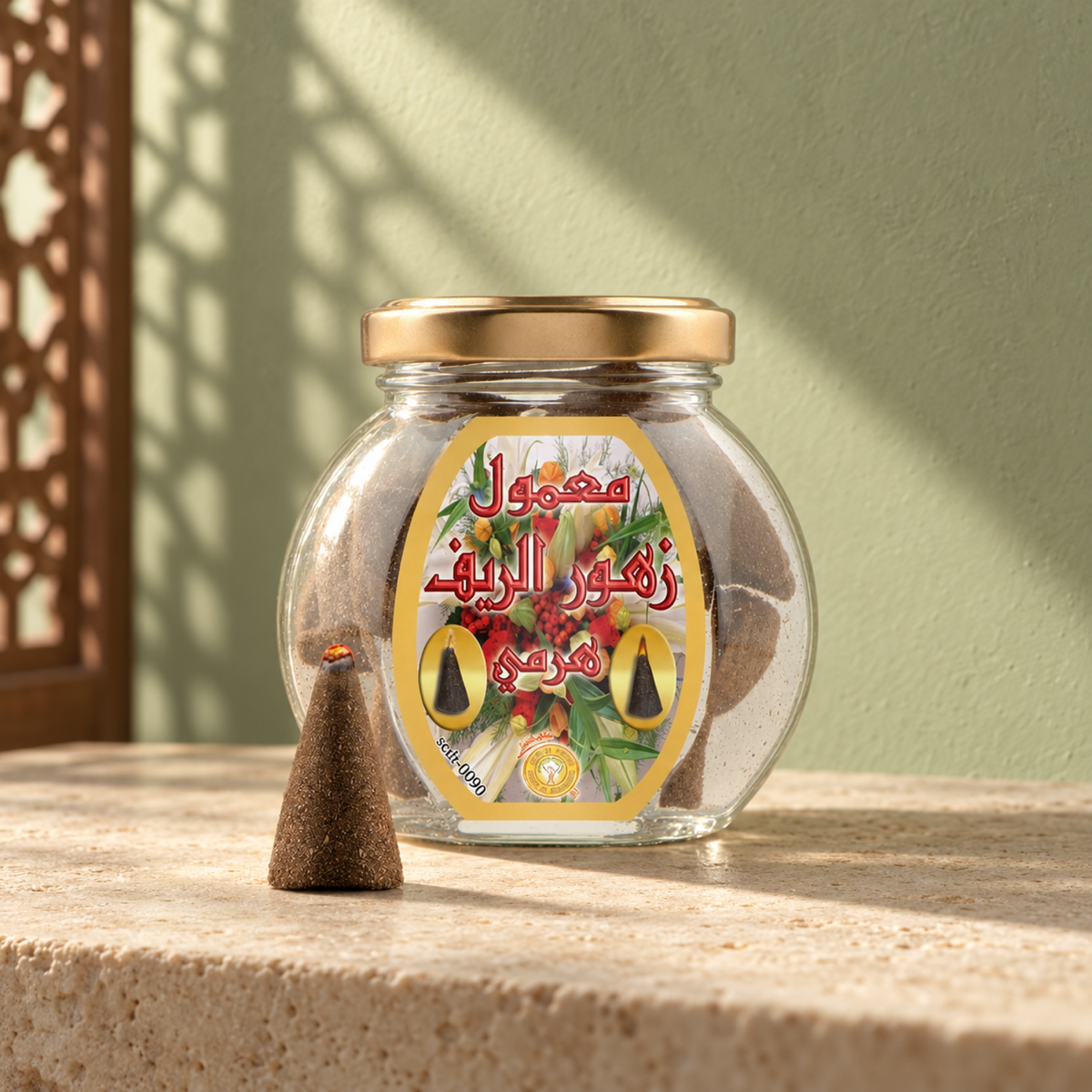 Zuhoor Al-Reef Pyramid Maamoul 50 g from Sedr Al-Khaleej; round glass incense jar with a floral label, gold lid and one cone on limestone against a pale sage wall.